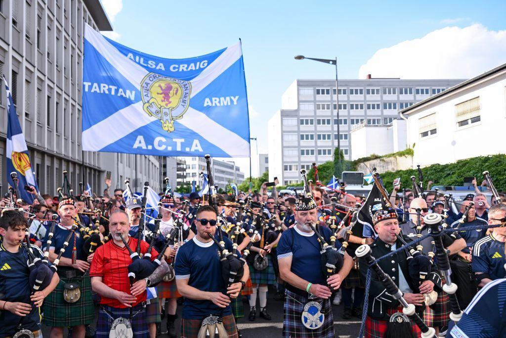 A large crowd of Scotland fans wearing Scotland tops and kilts marching through Cologne, led by bagpipers