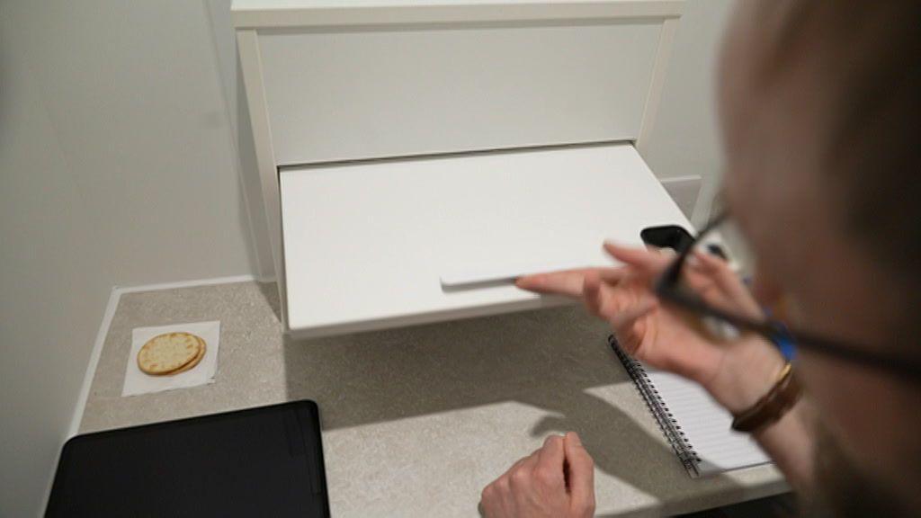A man's hand opening the hatch. Next to him is a note book and on the left-hand side of him are two crackers on a tissue.