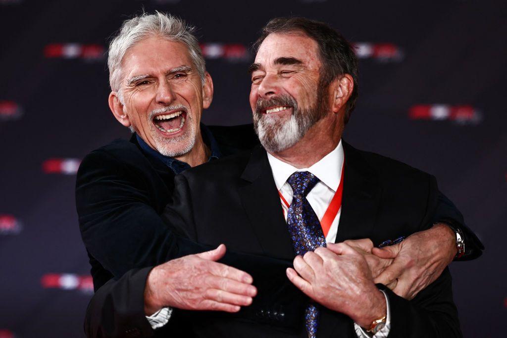 Damon Hill (left) grabs Nigel Mansell as they both laugh at the camera. Both men are wearing dark suits.