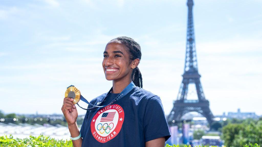 Naomi Girma holding her gold Olympic medal in front of the Eiffel Tower in Paris.