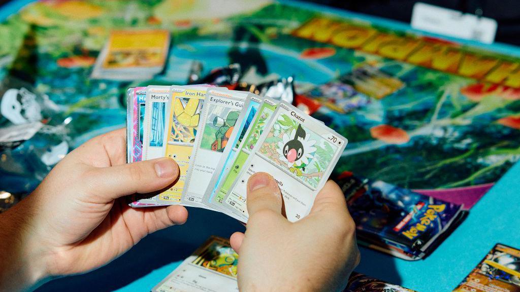 Someone holds Pokemon cards over a board 