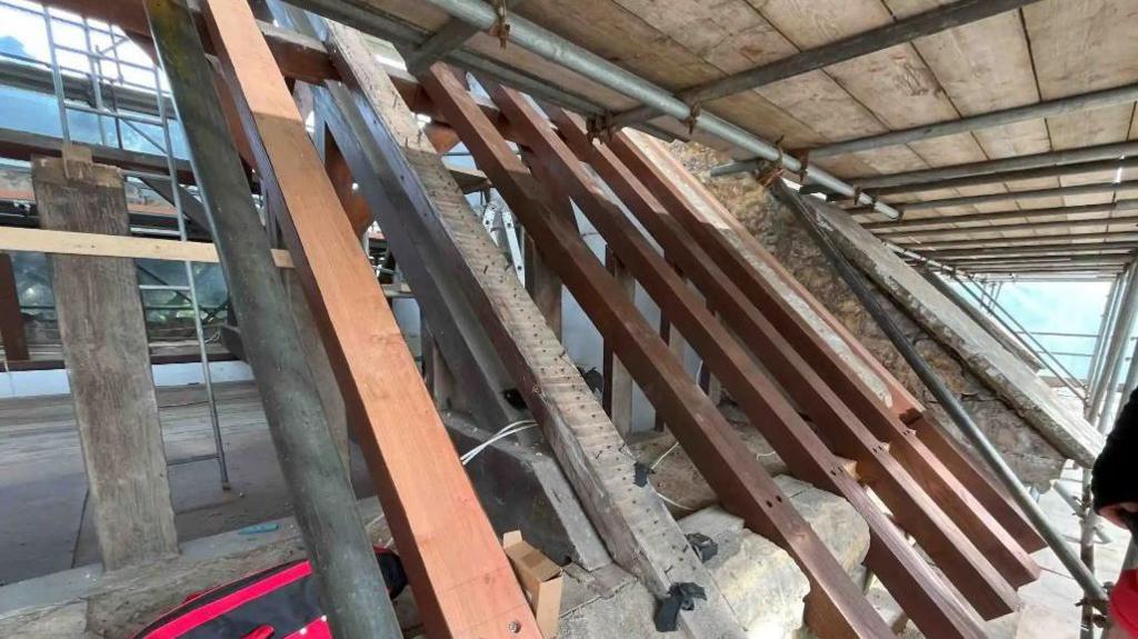 Exposed roof of St Nicholas of Myra Church with stone and wooden timbers arching across - the roof is under repair with scaffolding covering it.