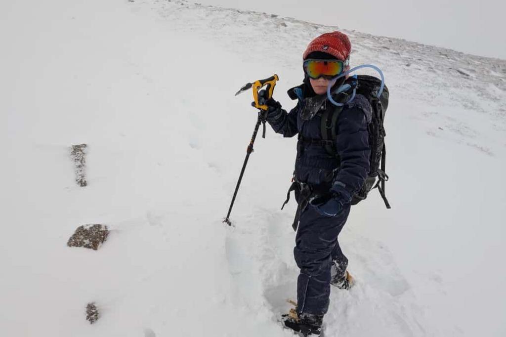 Rio in full snow gear, hat and ski goggles. He has a specialist walking stick and is surrounded by snow.
