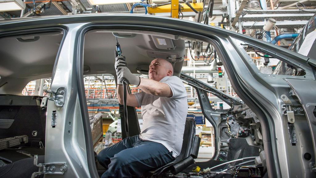 Stock photo shows a worker adjusting parts in a car factory in the UK