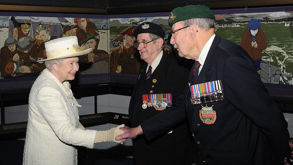 Queen Elizabeth II, dressed in a cream hat and jacket, meets D-Day veterans Frank Rosier and Eddie Wallace - who are dressed in military ceremonial dress - next to the the Overlord Embroidery aduring her visit to the D-Day museum as it marks its 25th anniversary on April 30, 2009 in Portsmouth.