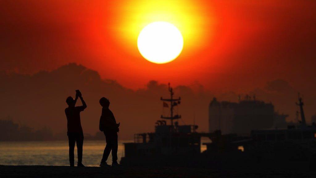 People taking photo of the sunrise are pictured with vessels anchored along the southern coast on April 2, 2021 in Singapore.