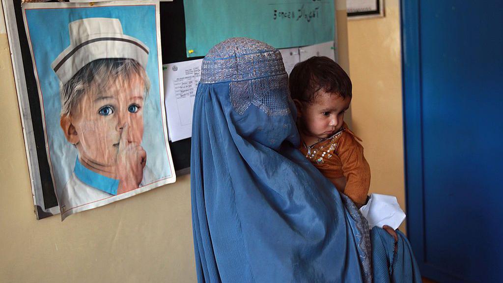 A mother and child await a medical check-up at a USAID-funded health centre on 7 September 2011 in Farza, Afghanistan. The mother is wearing a blue burka covering her head, face and body.