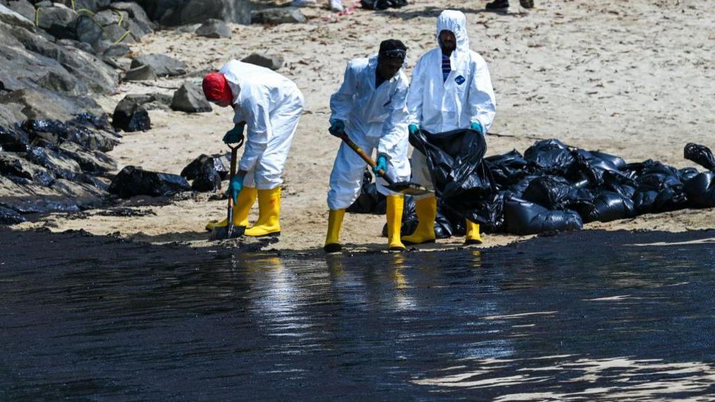 people cleaning up oily sand in protective clothing