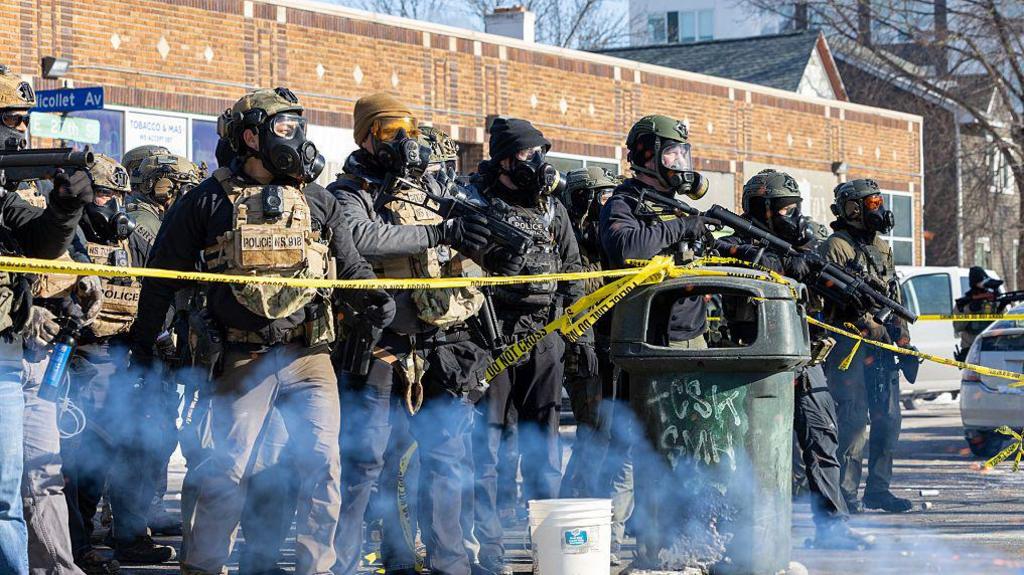 Ice agents, federal agents and law enforcement officers standing behind yellow police tape, facing protesters on Nicollet Avenue in Minneapolis