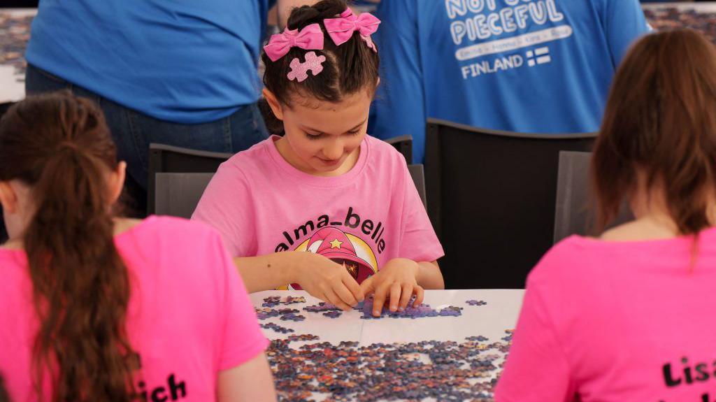 A girl wearing pink looking at jigsaw pieces