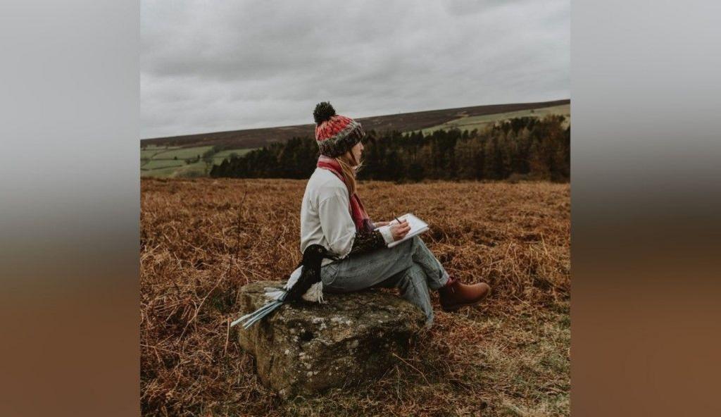 Ms Tennant sat in the countryside with a notepad and pen, looking out to the distance