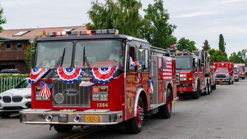 Fire trucks with red white and blue decoration drive down a street in Anchorage, Alaska, on July 4, 2024.