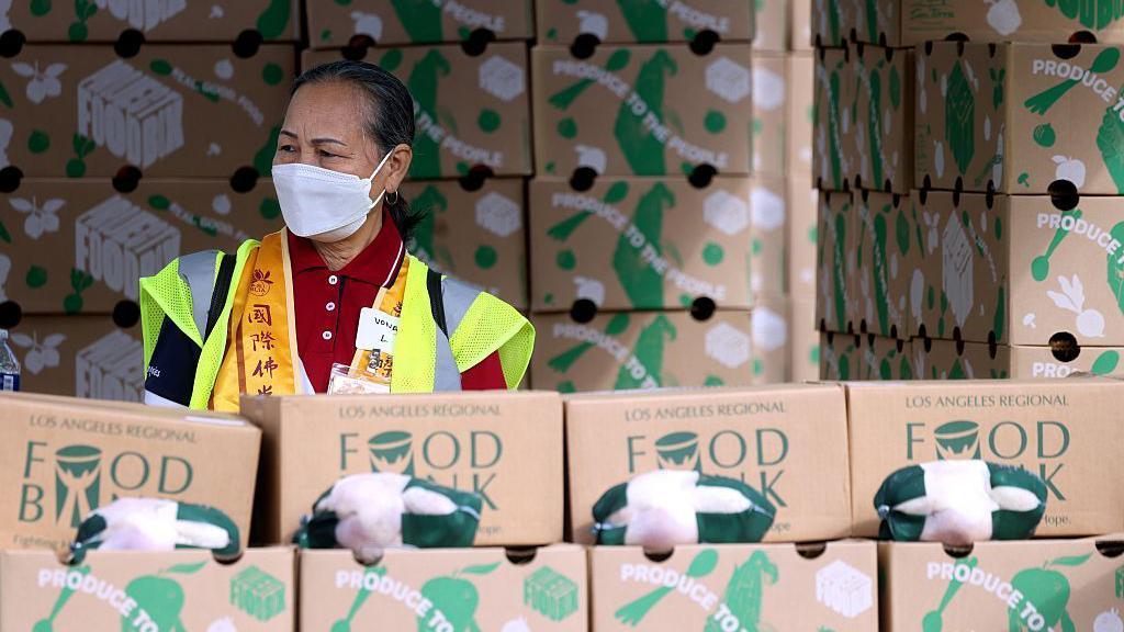 A worker in a mask stands in front of boxes of food to be distributed