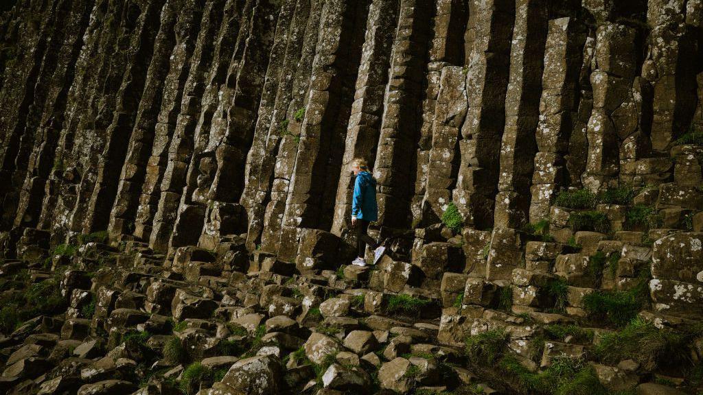 Tall columns from the Giant's Causeway with a person in a blue coat walking in front of them