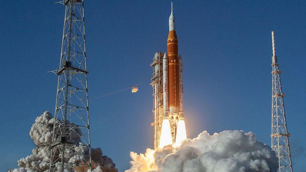 NASA's SLS Moon rocket lifts off from launch pad 39B at the Kennedy Space Center in the United States, carrying Artemis II astronauts Reid Wiseman, Victor Glover, Christina Koch, and Jeremy Hansen on a 10-day mission around the Moon. A rocket is taking off with flames coming from the bottom of it and smoke is all around the bottom too.