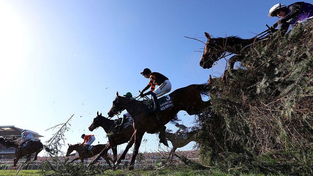 Four horses jump over a fence at the Grand National with Nick Rockett in the lead