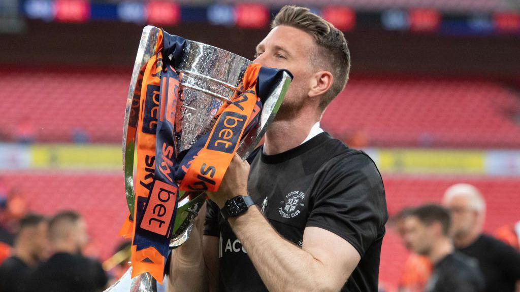 Rob Edwards hold and kisses the Championship play-off trophy, which has orange and dark blue ribbons, at Wembley Stadium