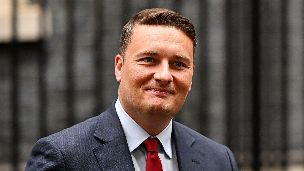 wes Streeting wearing a blue blazer, white shirt and red tie