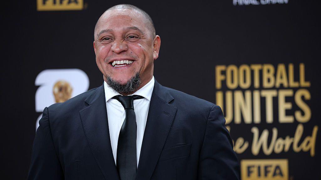 Roberto Carlos smiles for a photo while wearing a suit at the Fifa World Cup draw