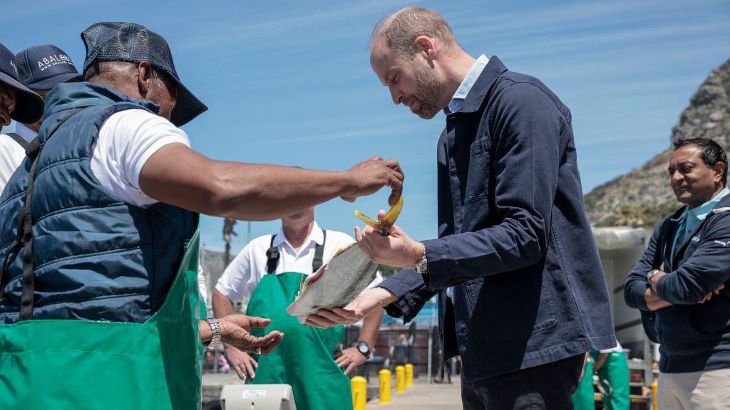 Prince of Wales is handed a fish as he speaks to a local fisherman in Cape Town