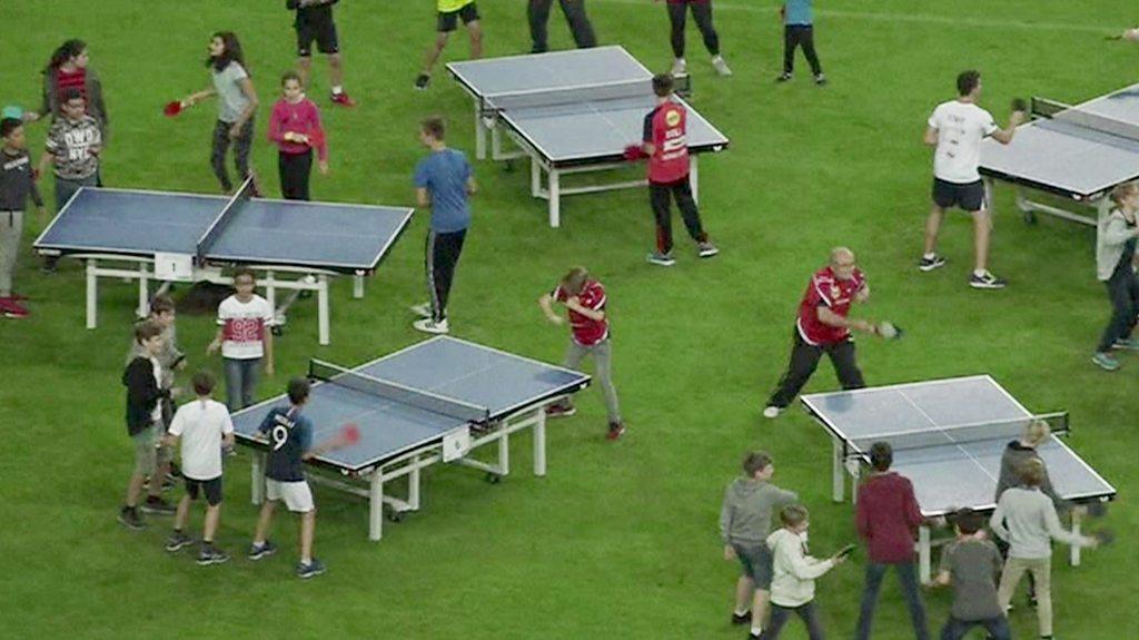 A group of children playing table tennis on different tables.