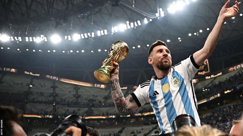 Messi is lifted by his team-mates, holding the World Cup