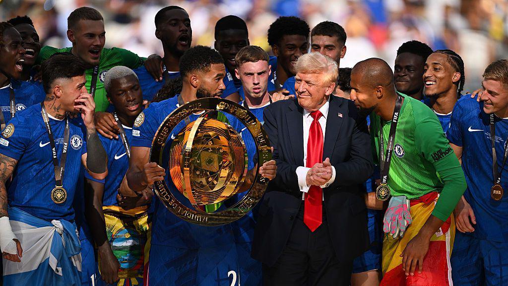 Reece James of Chelsea holds the Club World Cup trophy after the team's victory over PSG. US President Donald Trump is standing with the team at MetLife Stadium, New Jersey