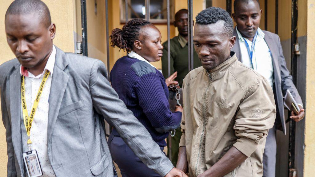 Collins Jumaisi Khalusha in handcuffs being escorted through court by a man in a grey suit, police officers in background