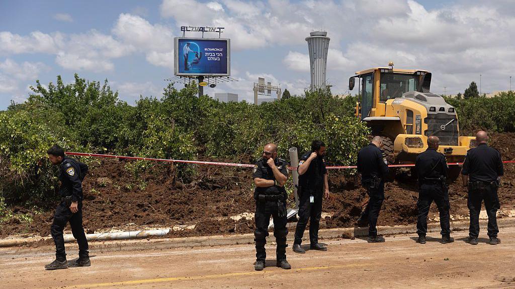 Police officers guard as a tractor works at a scene where the ballistic missile landed