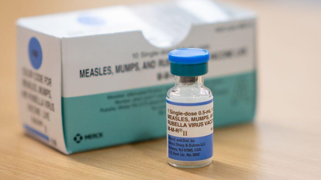 A photograph of a measles vaccine in a glass vial with blue label