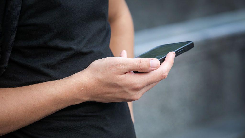 A man in a black t shirt holds a mobile phone 