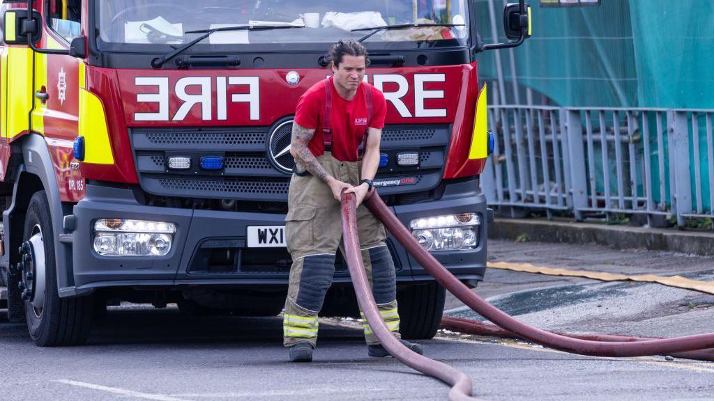 A firefighter moves hosepipes after a fire at a block of residential apartments