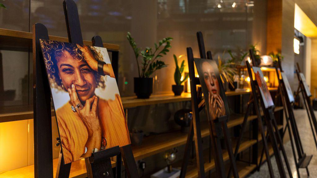 Five photos of models, each on an easel, are stood in a row at an exhibition.