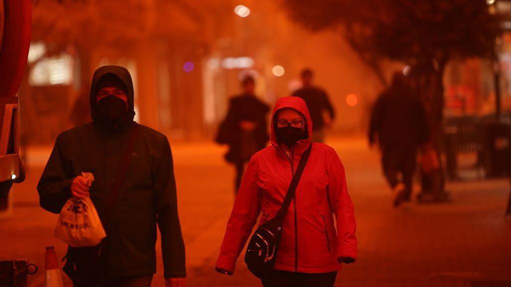 people walking through Saharan dust storm red sky.