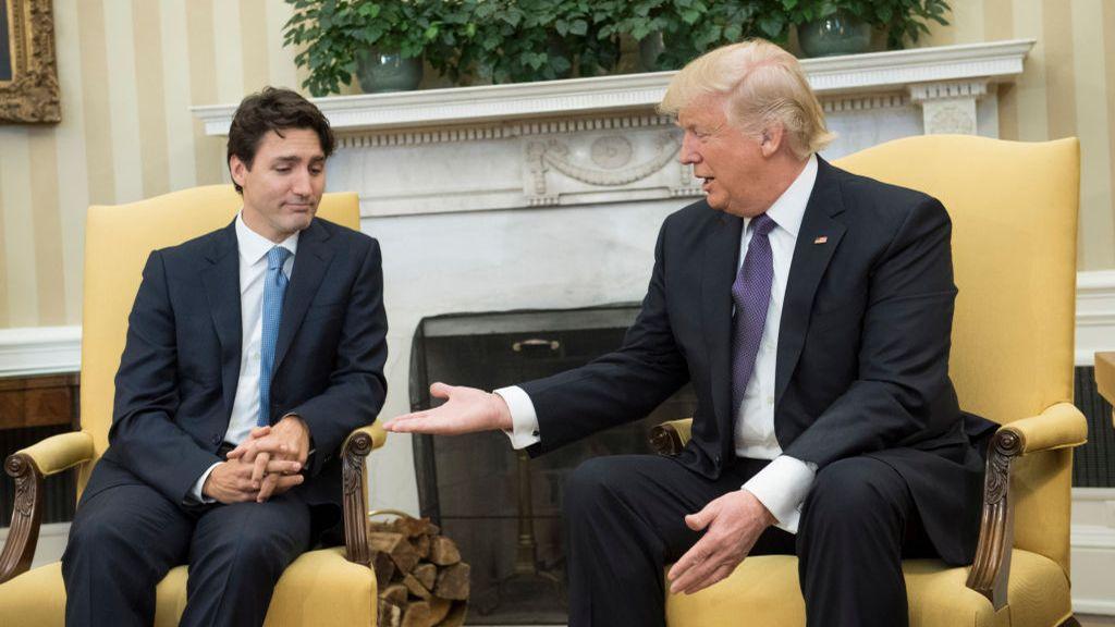 President Donald Trump extends his hand towards Prime Minister Justin Trudeau of Canada during a 2017 meeting at the White House. Trudeau has his eyes cast down and his own fingers knotted together.