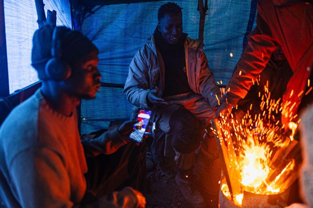 South Sudanese migrants gather around a fire to warm up under a tent at a makeshift camp.