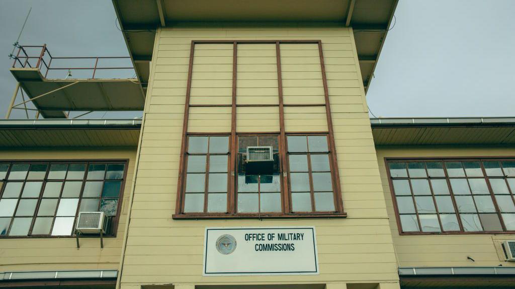 A yellow building has a sign that reads "office of military commissions"