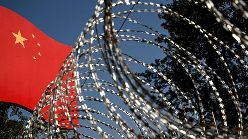 This photograph taken on January 14, 2023, shows a part of a border wall between China and Myanmar with barbed wire and a Chinese national flag, in Ruili, west Yunnan Province