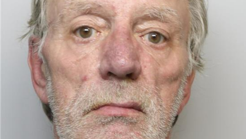 A mugshot of a middle-aged man with grey hair and grey stubble. He has a serious expression on his face.