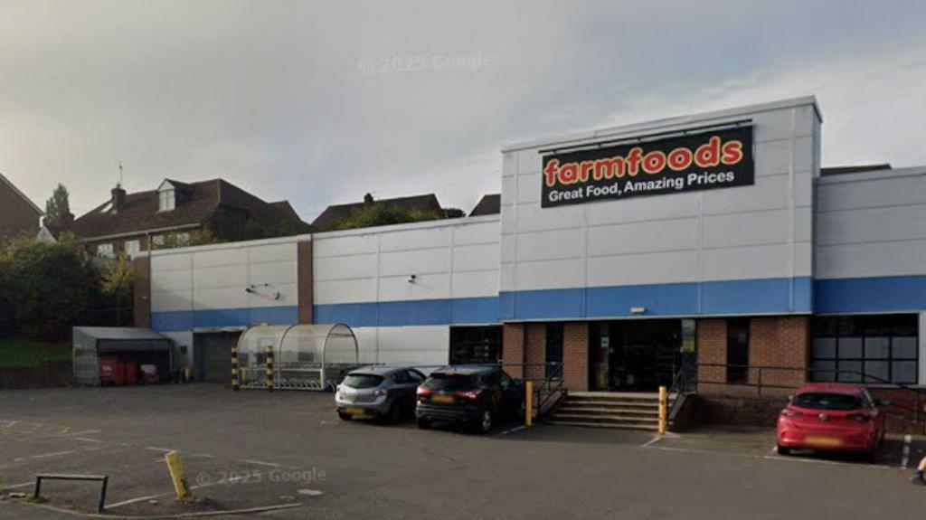 A large grey building with the words Farm Foods in red lettering and a car park in front