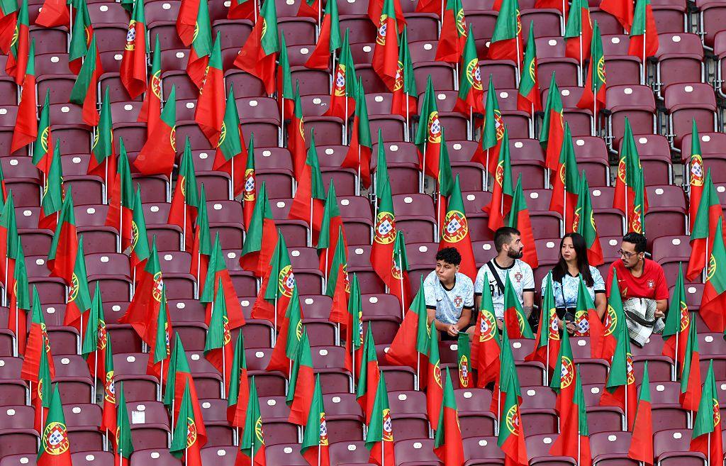 Four Portugal fans sit in an empty stadium filled with Portuguese flags neatly placed between the seats.