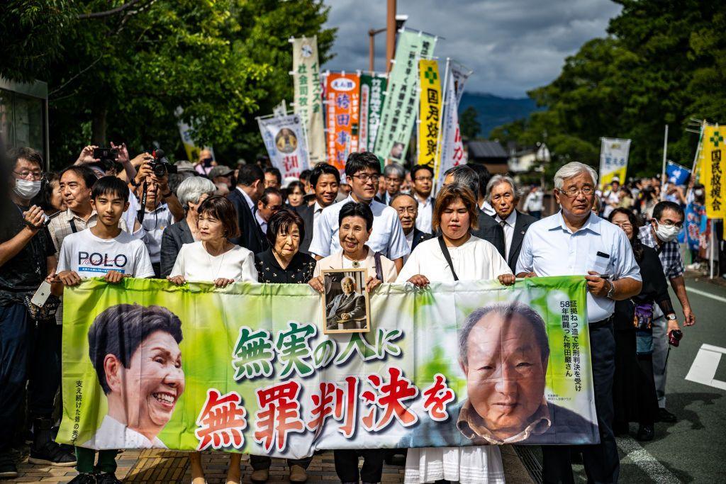 A crowd of people holds a banner reading "innocent man, not guilty verdict" alongside a picture of Iwao Hakamada