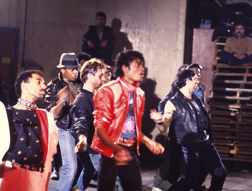 Michael Jackson in the video for Beat it, wearing red leather jacket and black jeans, surrounded by dancers