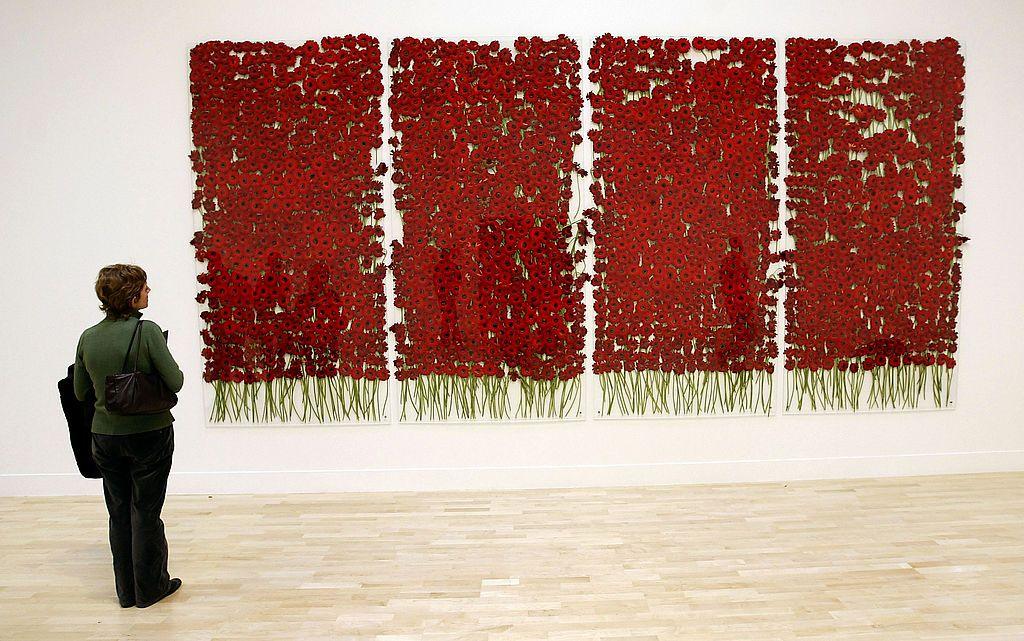 A woman looks at four wall hangings made up of deep red poppies