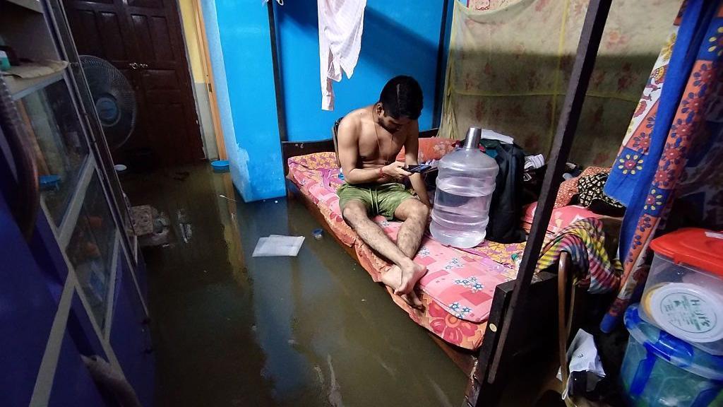 A man sits inside a house, surrounded by floodwater after heavy rain in India's Kolkata city