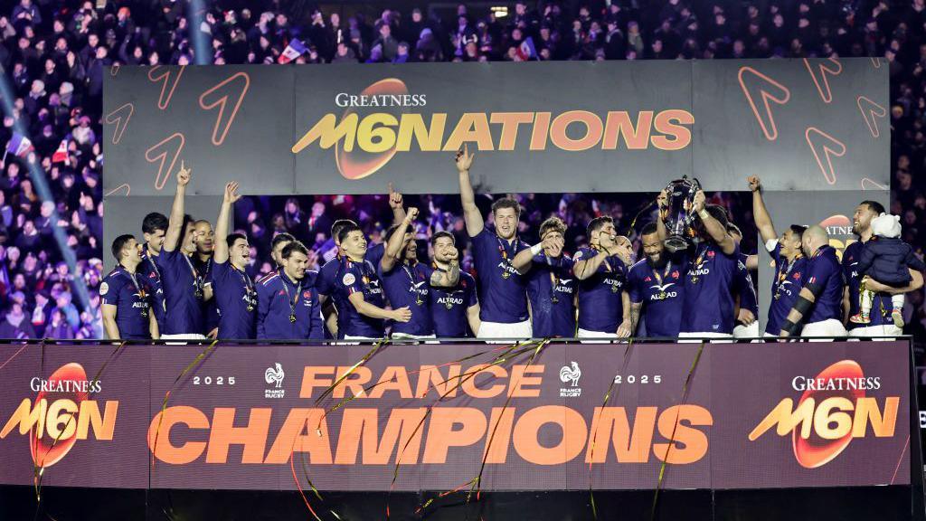 the french rugby team celebrating their six nations win in blue kits with one player holding up the trophy