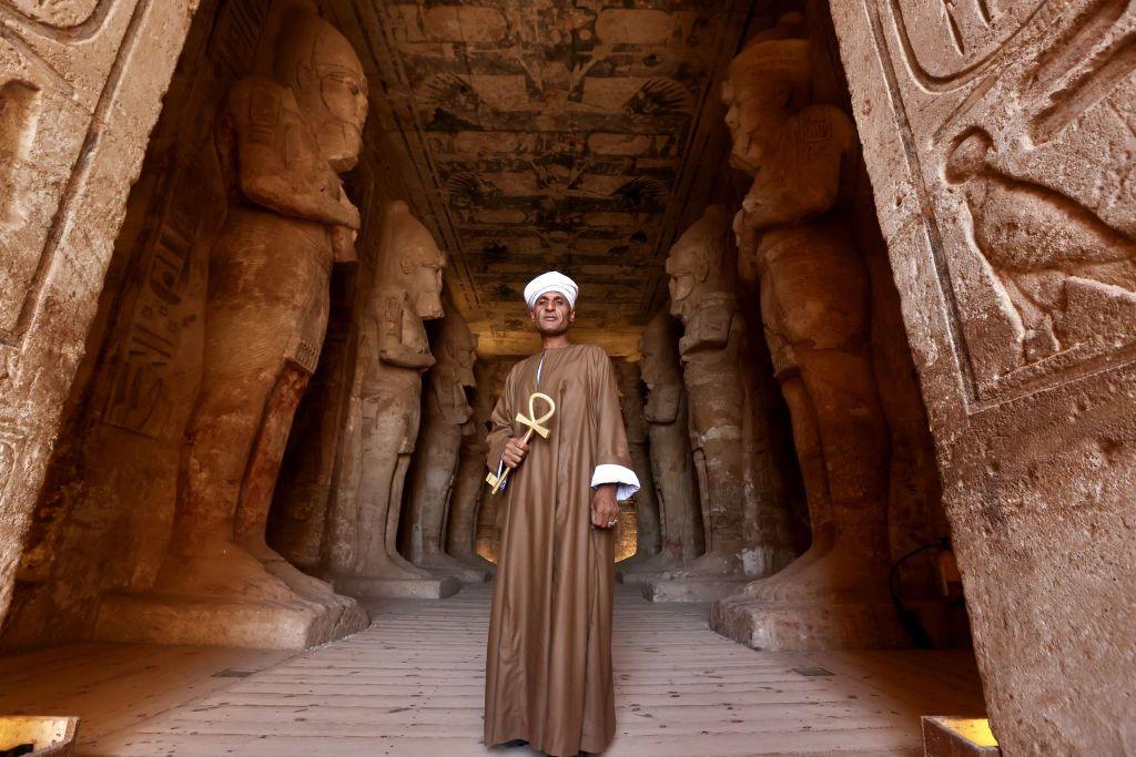 A man in brown robes stands at the entrance to an ancient Egyptian temple. 