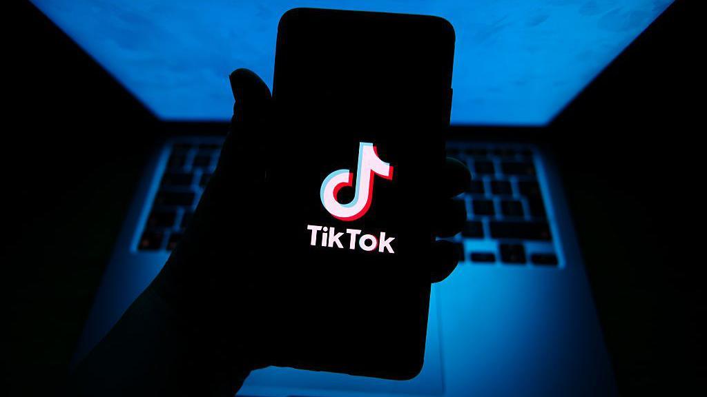 TikTok logo shown on a smartphone which is being held above a laptop