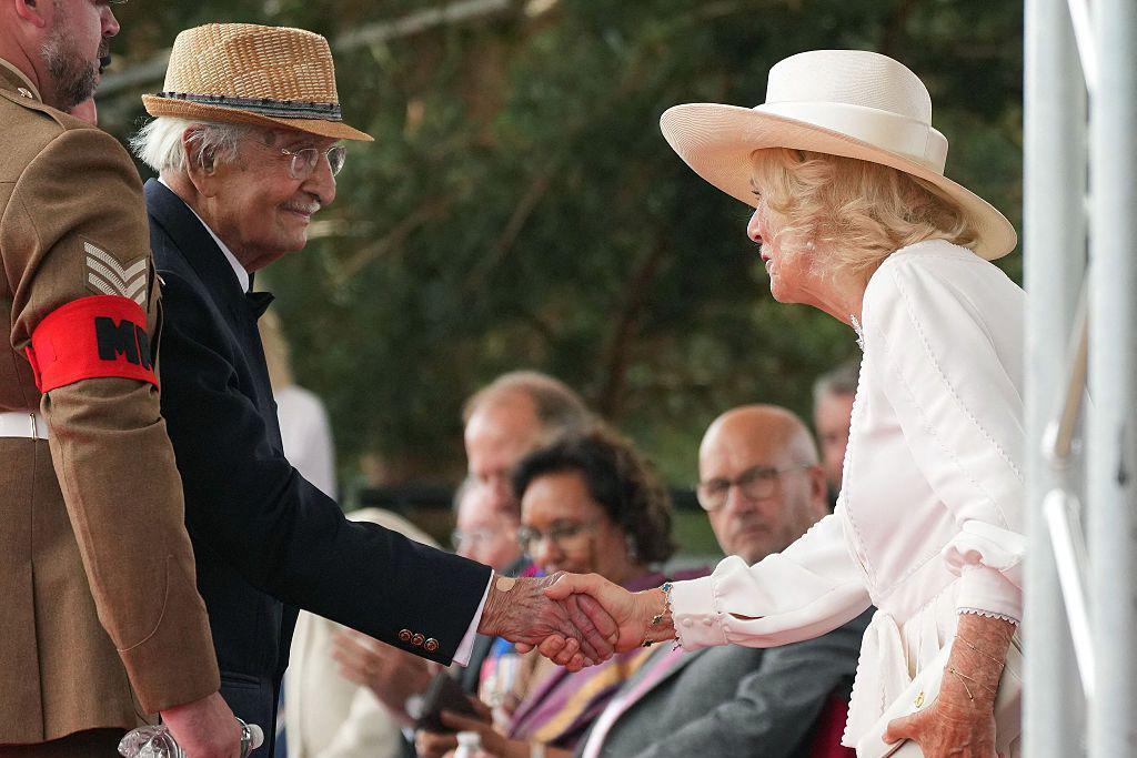 Yavar Abbas (left) smiles as he shakes hands with Queen Camilla (right)