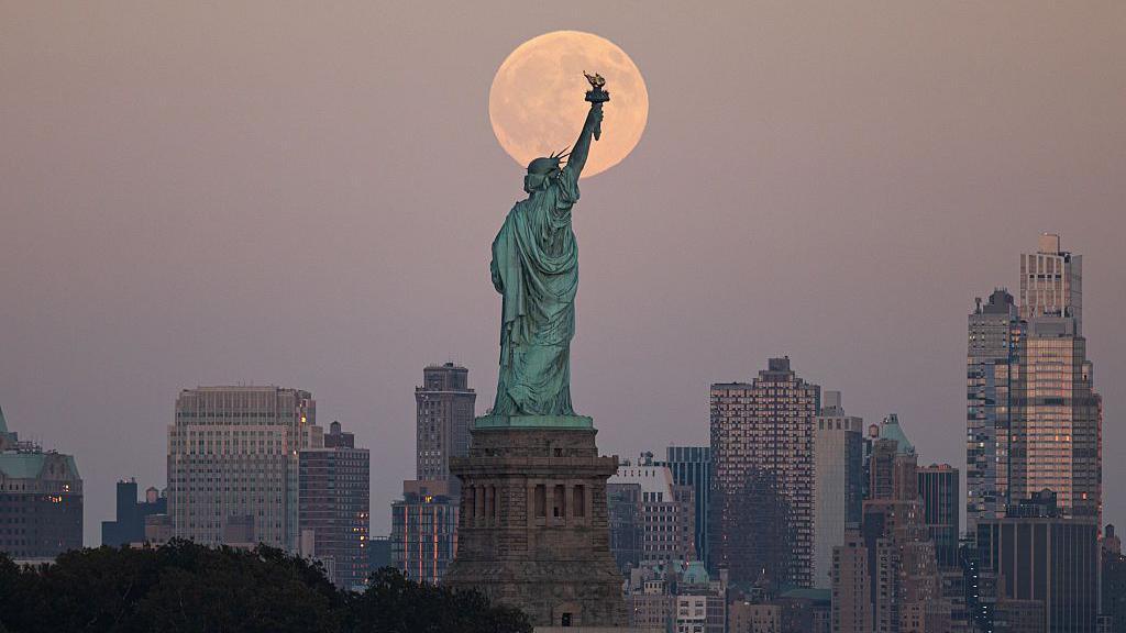 The orange Moon behind the famous statue of Liberty in New York